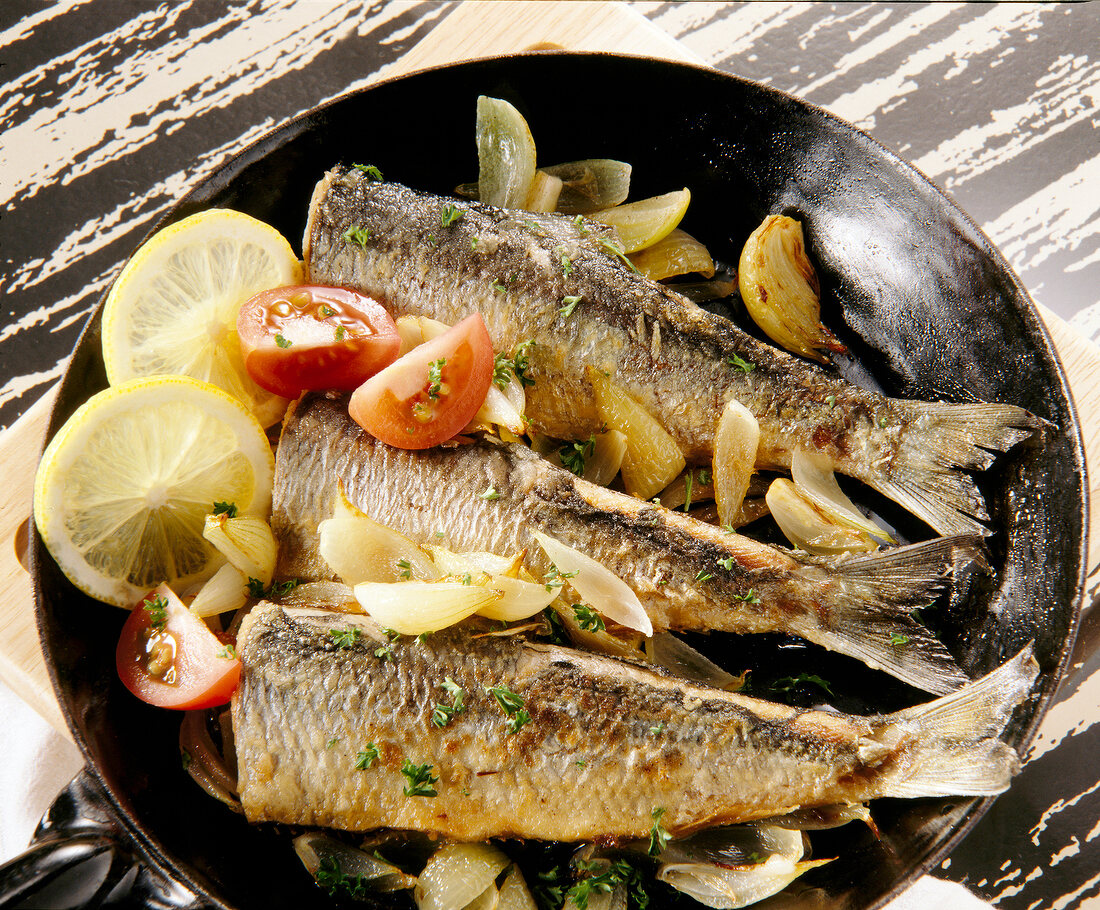 Close-up of herrings with onions, tomatoes and slices of lemon in pan