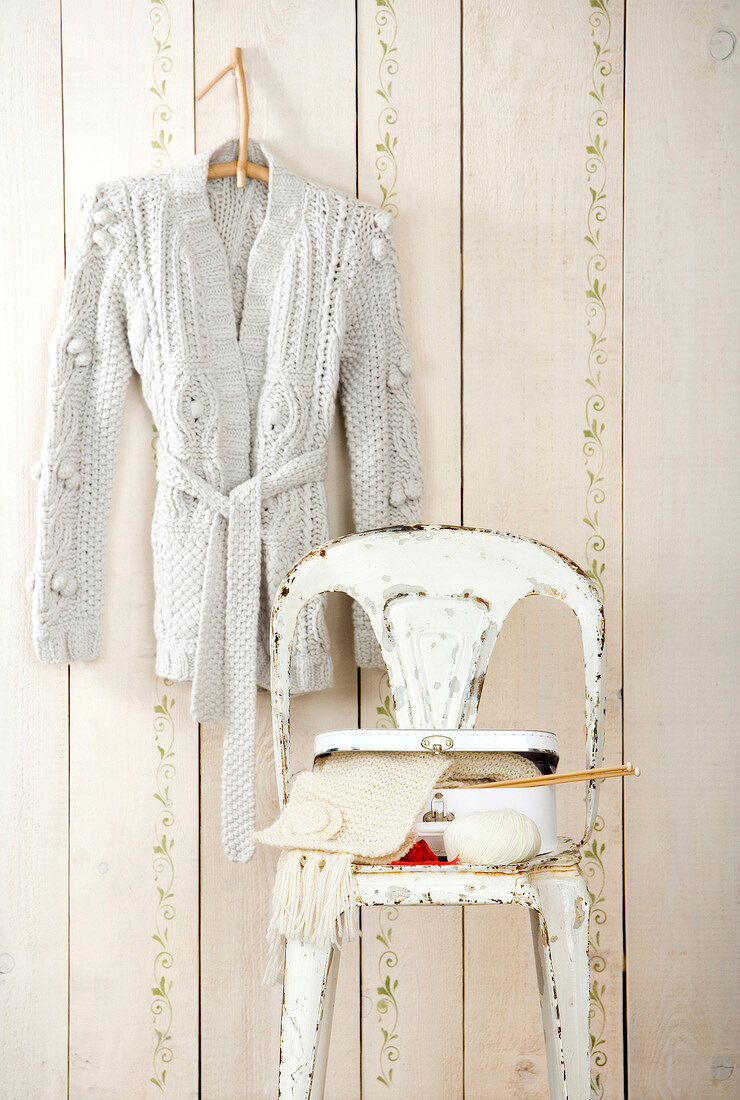 Cream woollen cardigan on hanger and suitcase on chair