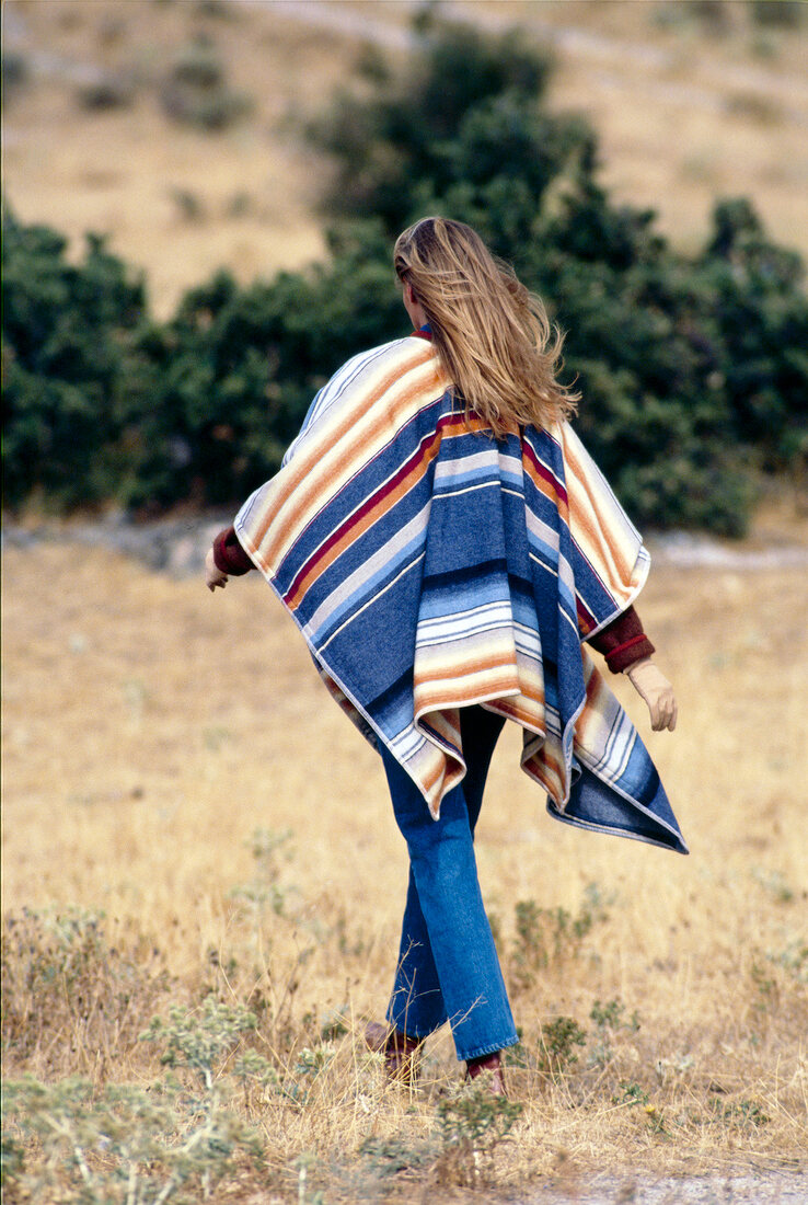 Rear view of blonde woman wearing Indian cape and blue jeans walking in prairie