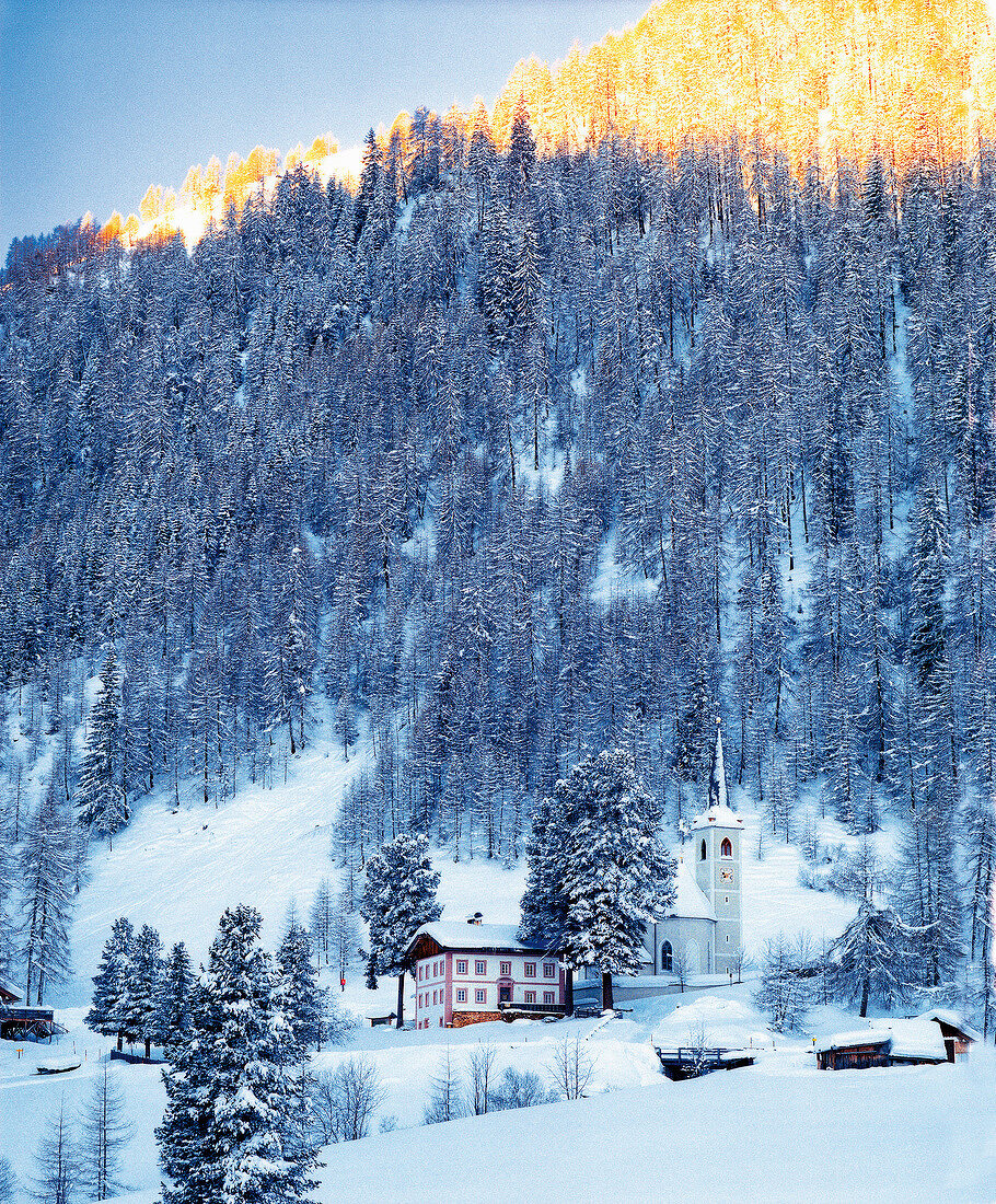 View of chapel on the hillside with pine trees and snow