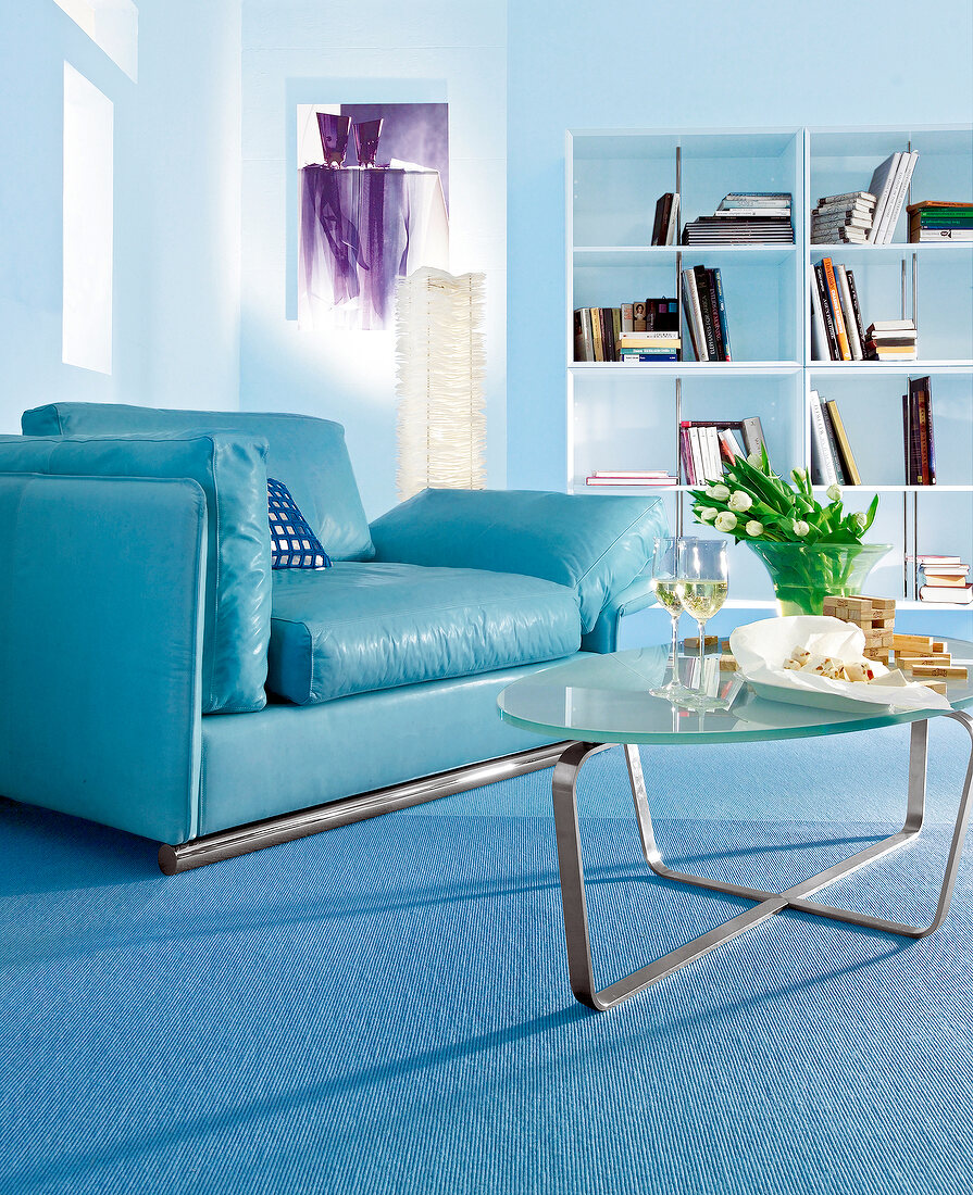 Living room in blue with leather armchair, bookcase, glass table and flower vase