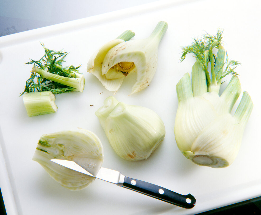 Removing stems and green of fennel bulb on chopping board