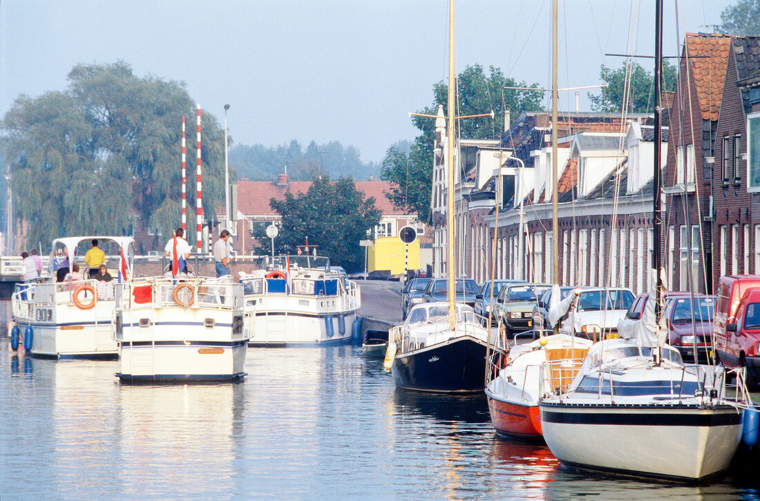 Houseboats moored at harbour in front of parked cars and facades, Amsterdam, Netherlands