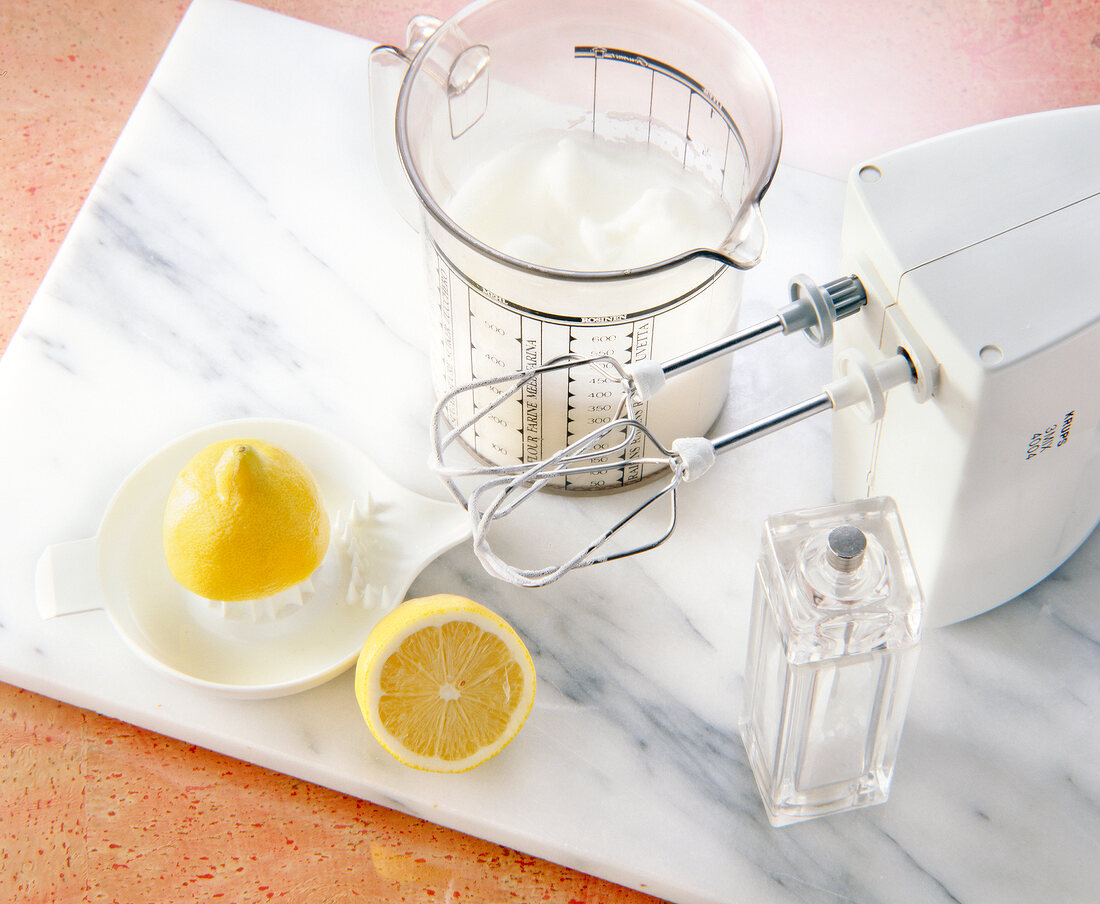 Beaten egg white in measuring cup, halved lemon, blender and salt spreaders on board
