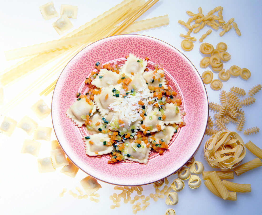 Ravioli with carrots and leek vegetables on plate and different types of pasta on side