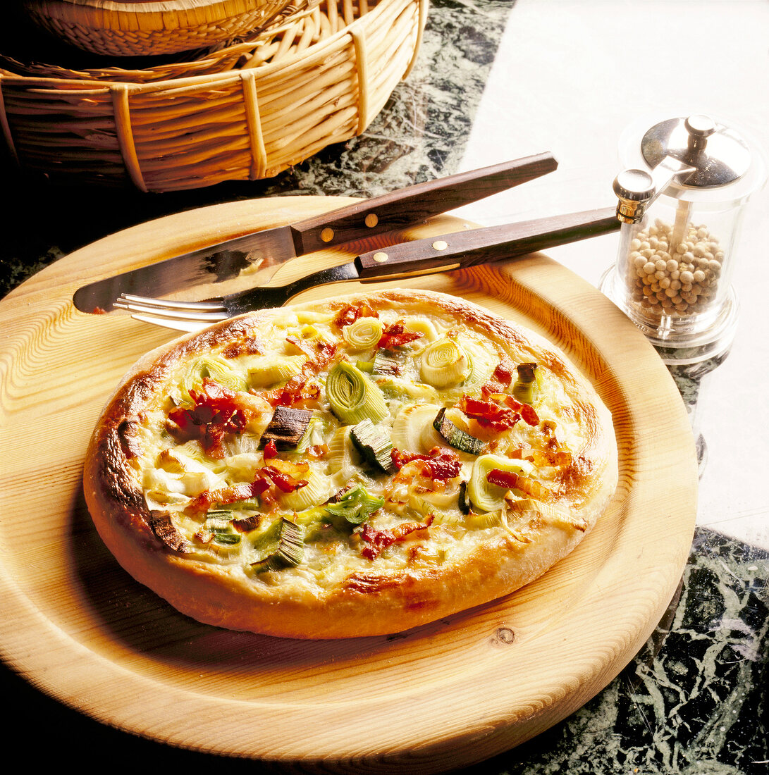 Yeast dough flatbread with leeks, onions, bacon and cheese in serving dish