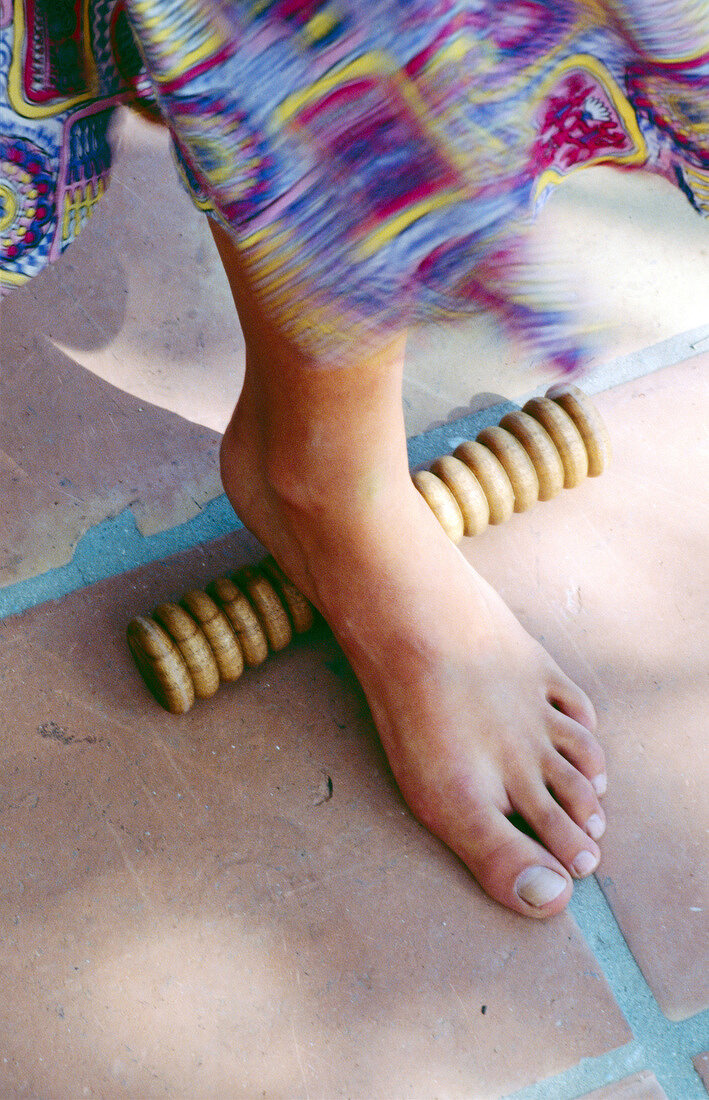 Close-up of woman's foot rolling over wooden foot roller massager