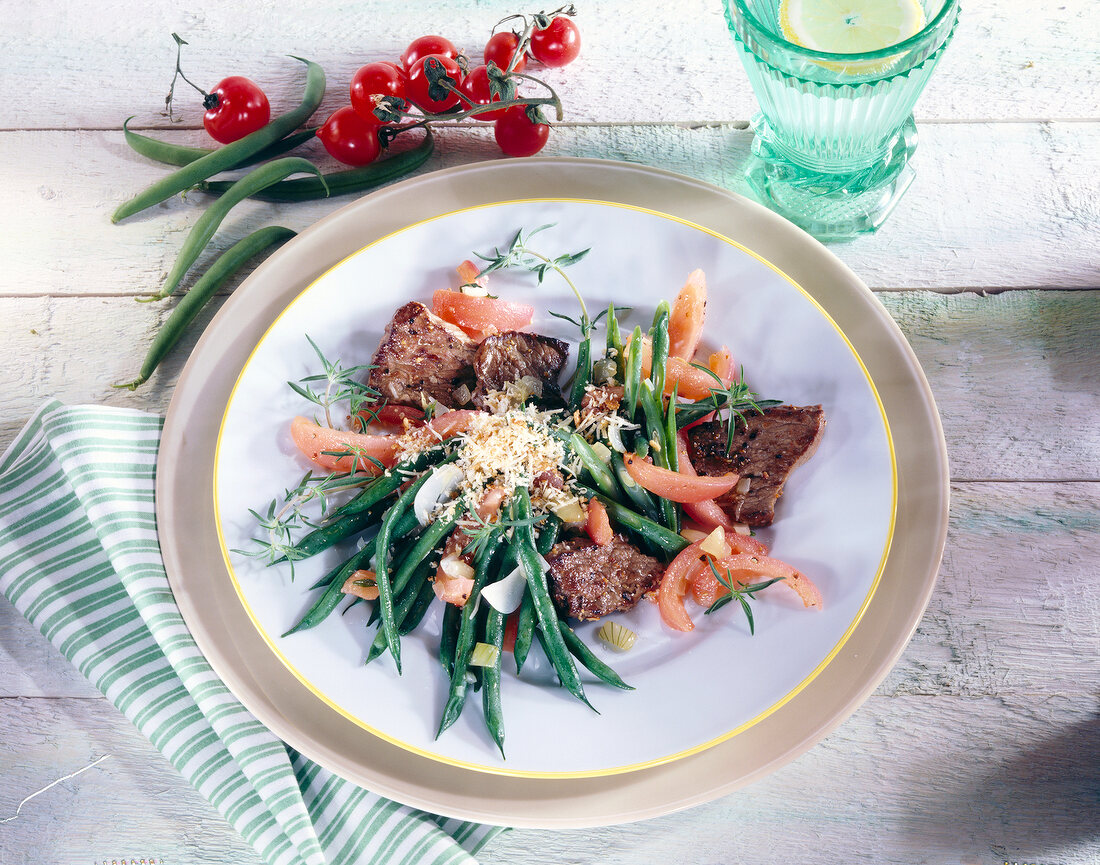 Beef slices with stir fried beans and tomatoes garnished with parmesan cheese