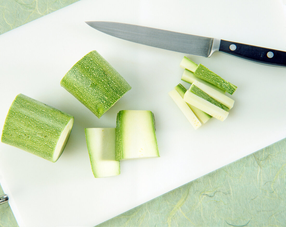 Sliced zucchini with kitchen knife on white chopping board