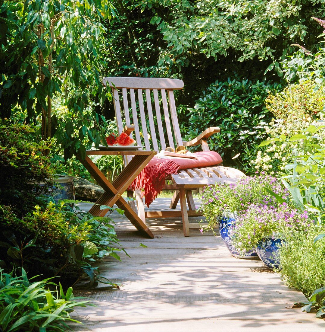 A wooden lounger and a table in a summery garden