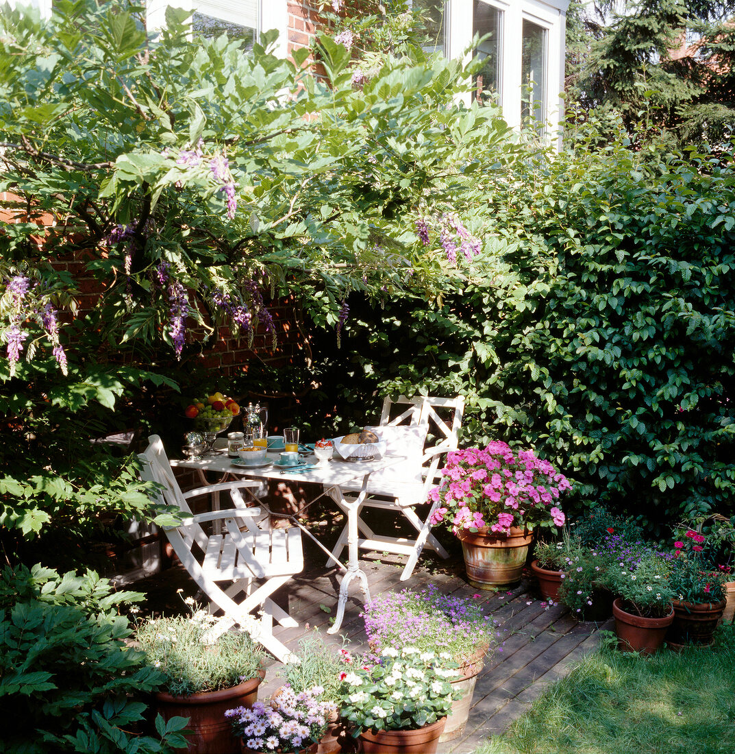 Sitzplatz im Garten mit weißen Moebeln, Hecke und vielen Blumen