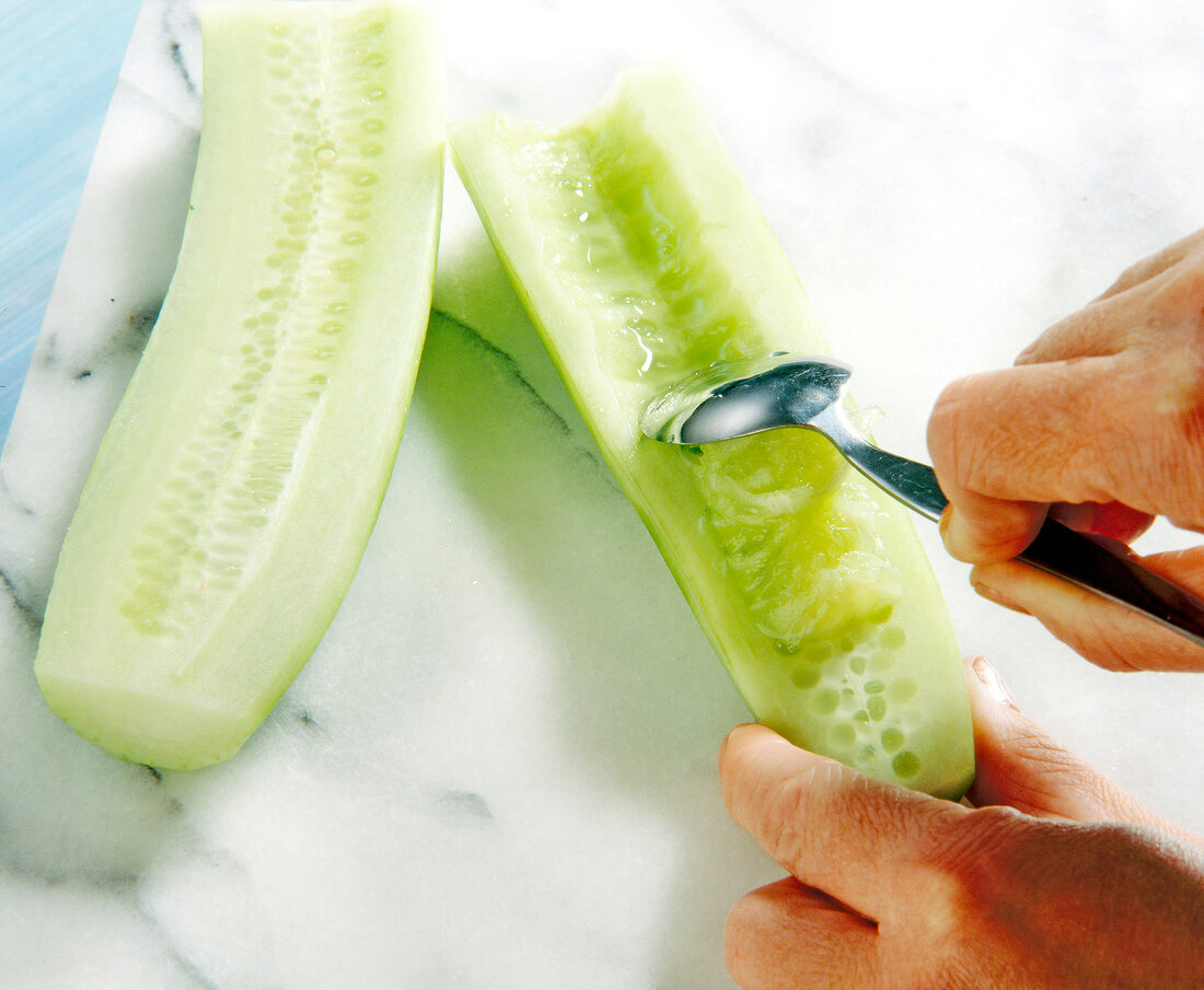 Close-up of seeds being scraped from cucumber with spoon