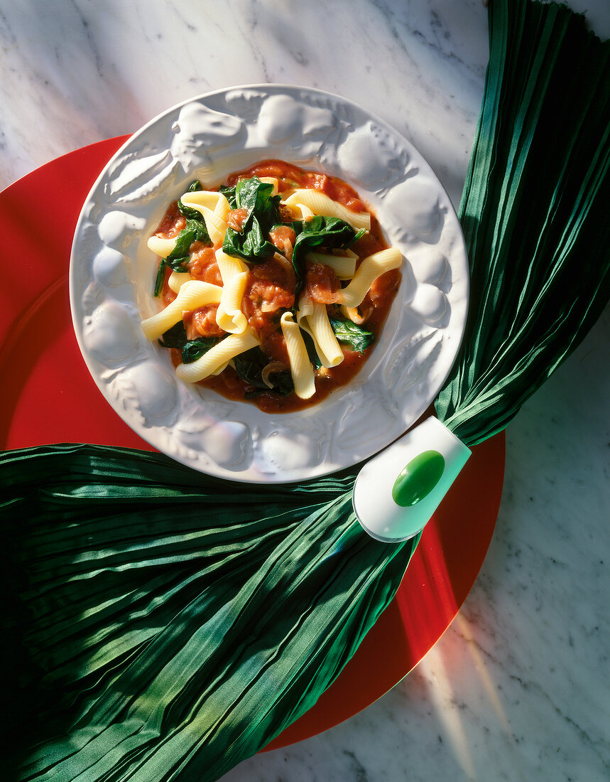 Pasta with tomato sauce, spinach and ham on plate, overhead view