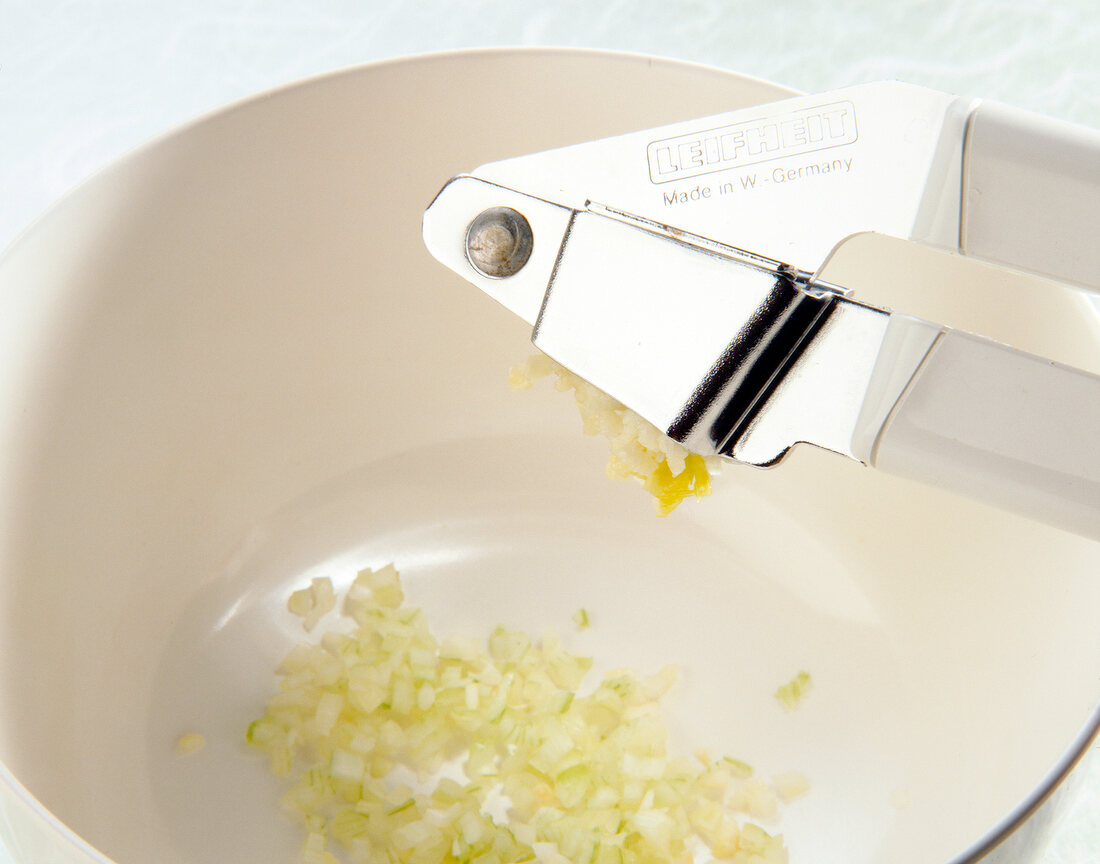 Close-up of garlic being crushed with garlic press in bowl