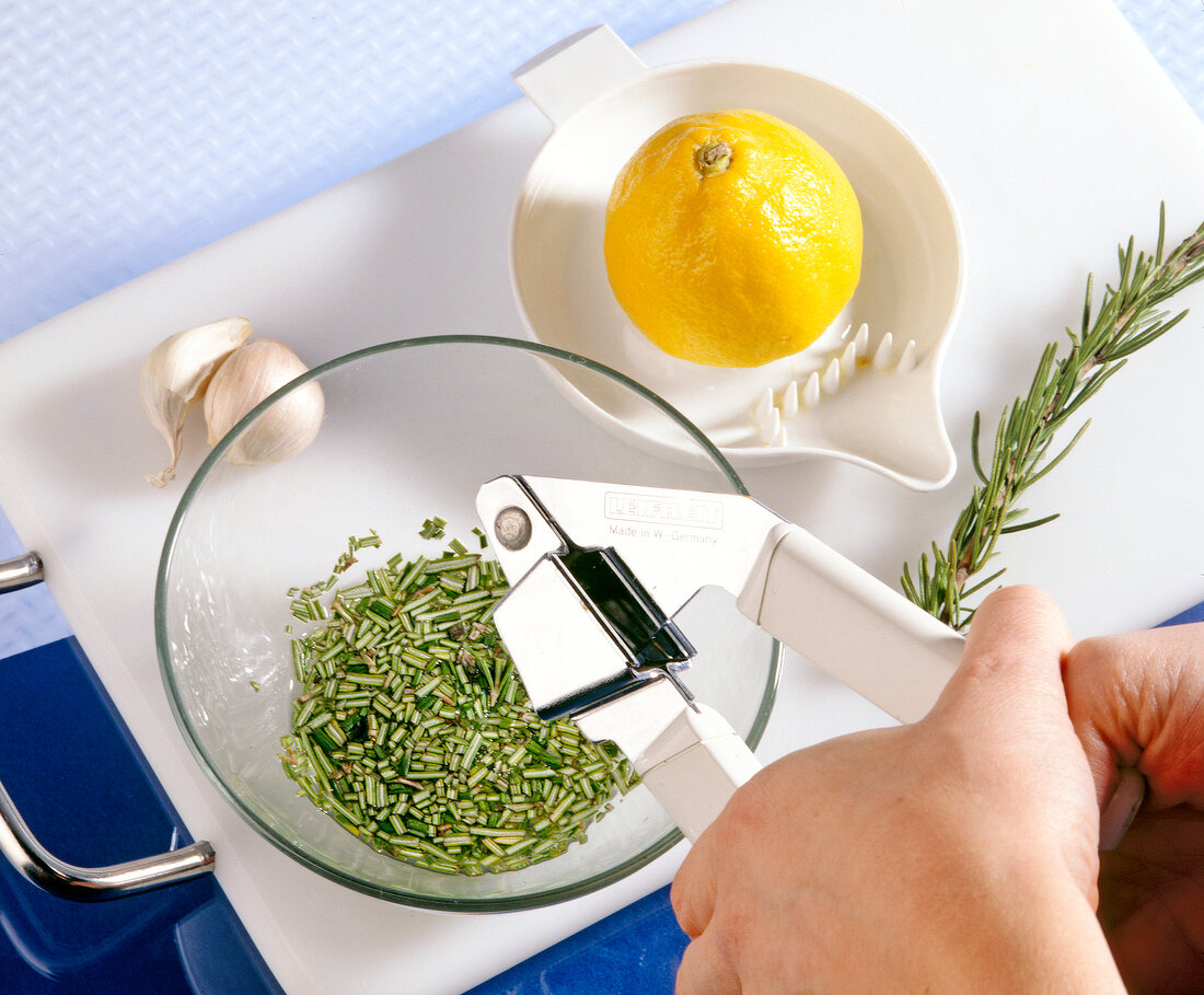 Rosemary being crushed with garlic press