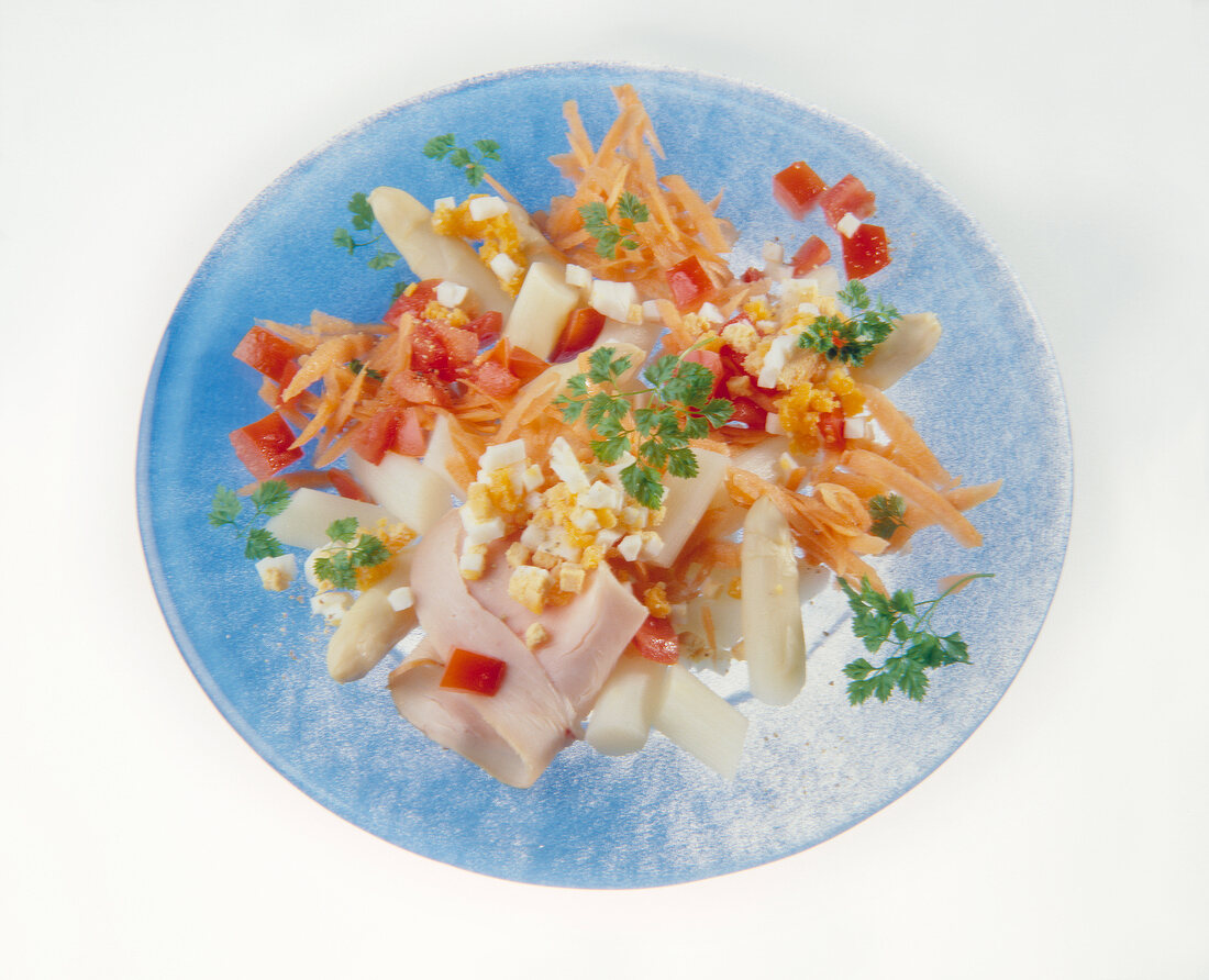 Spargelsalat mit Ei, Tomaten, Möhren und Putenbrust auf Teller in Blau