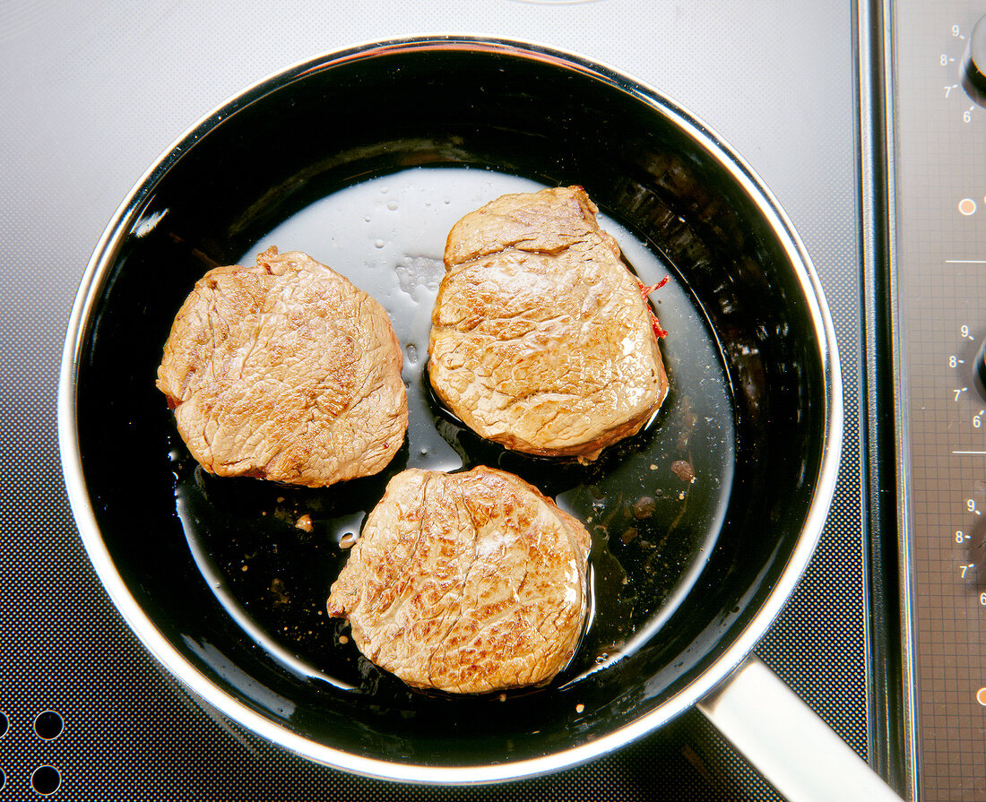 Close-up of three pieces of meat in pan