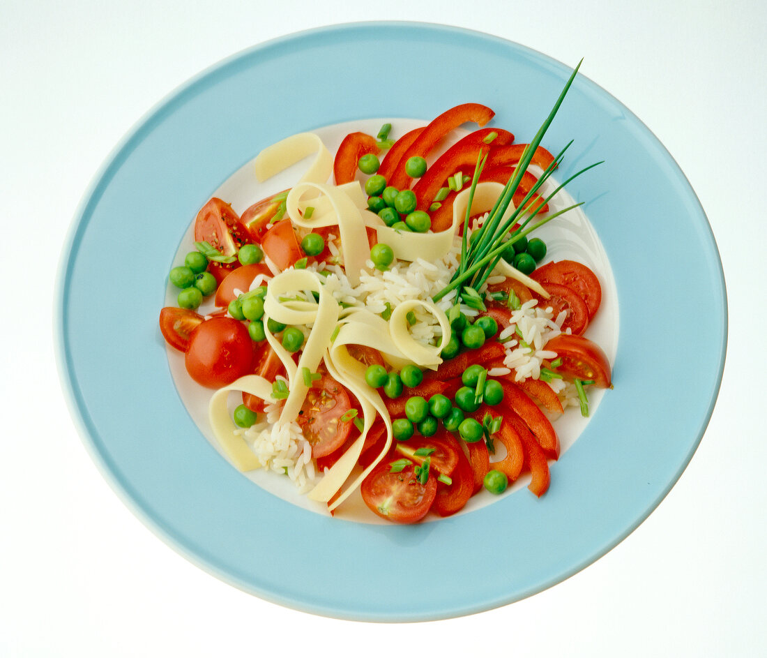Rice salad with tomatoes, peppers, cheese, peas and chives on plate