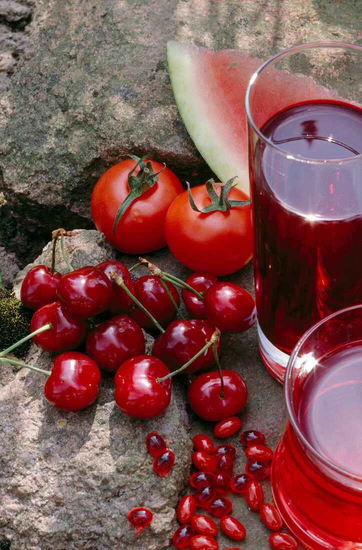 Close-up of cherries, tomatoes, slice of melon and glasses of fresh juice
