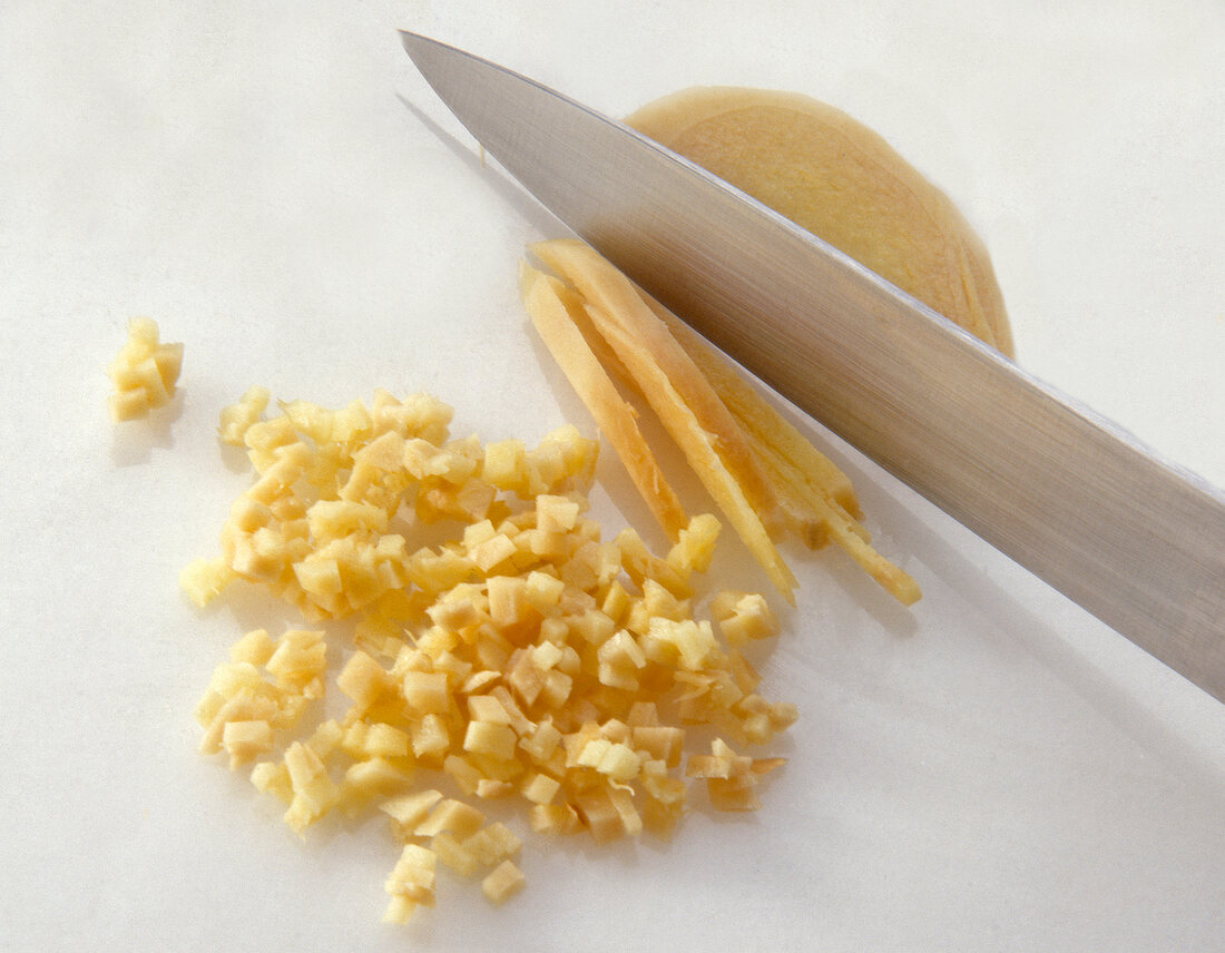 Ginger being chopped into small cubes with knife