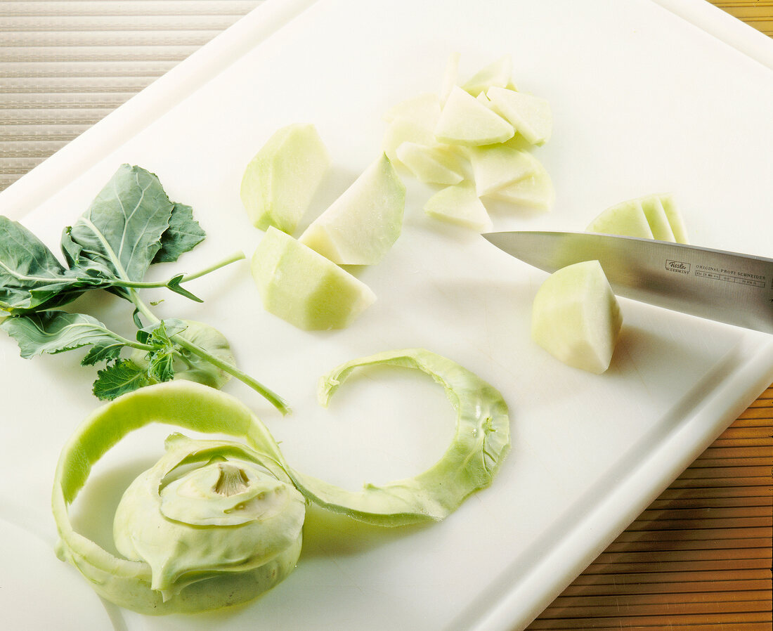 Kohlrabi being cut off with knife on chopping board