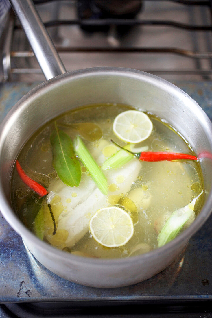 Fish fillet being boiled with lemon, chilli peppers and bay leaves in cooking pot