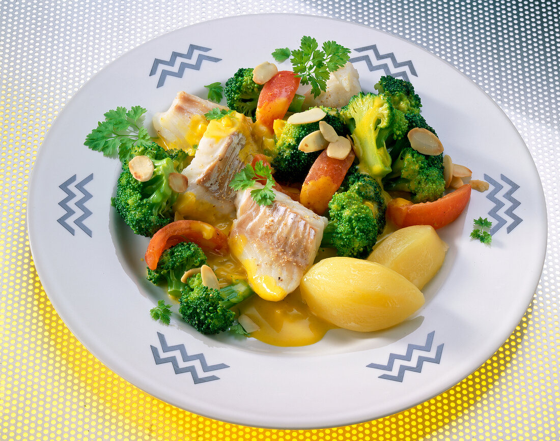 Cod fillet with broccoli, tomatoes, potatoes and flaked almonds on plate