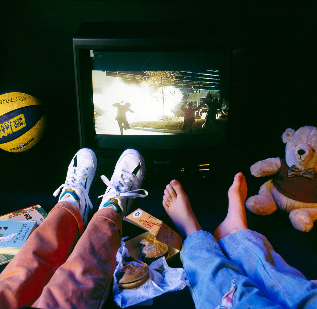 Children's' feet in front of television with half eaten muffins, scattered books and teddy