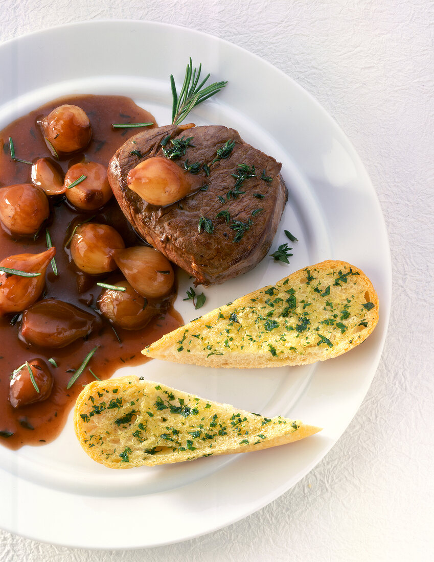 Beef tenderloin with shallot sauce and baguette with herbs on plate