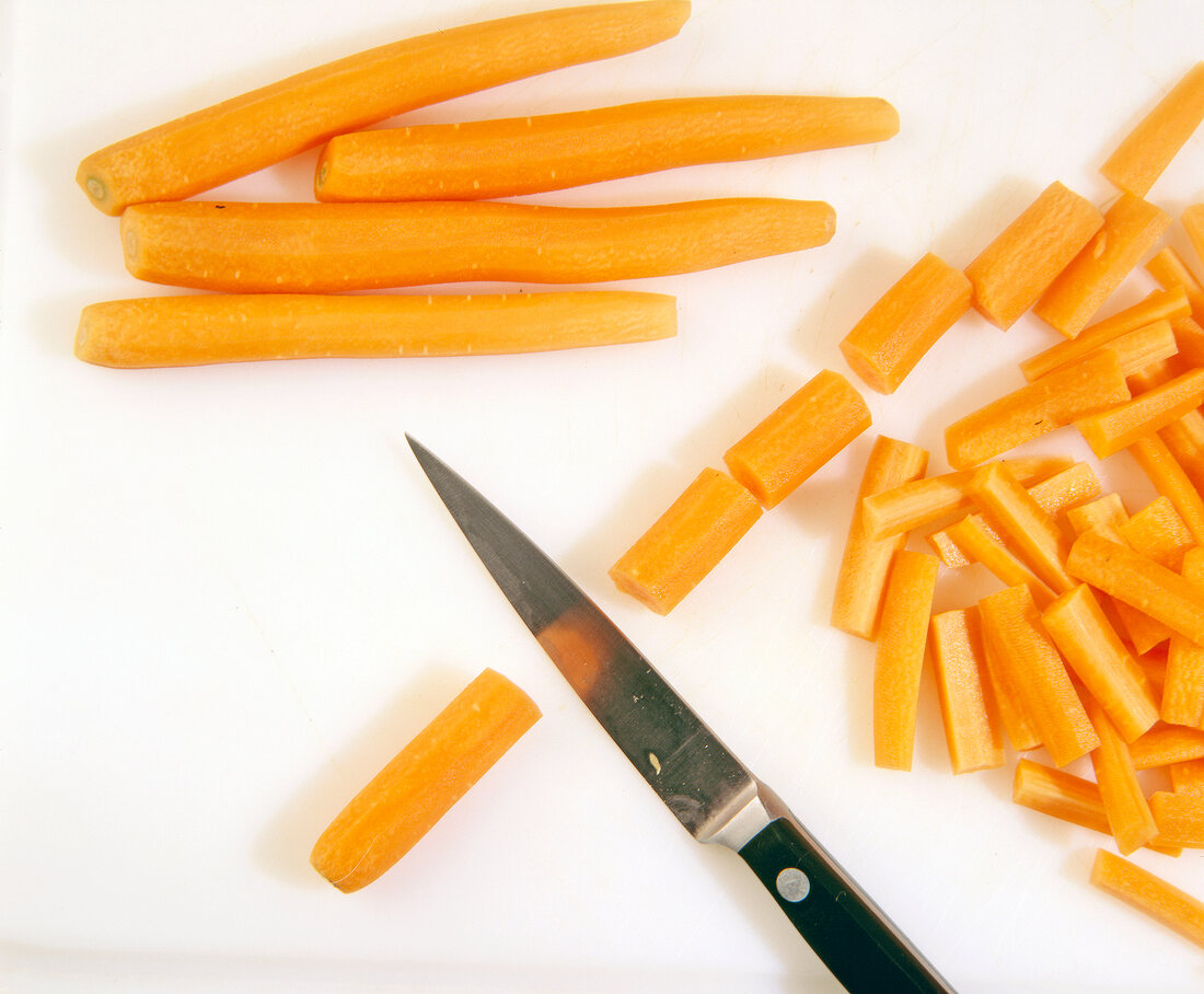 Peeled carrots cut to small pieces with knife on cutting board