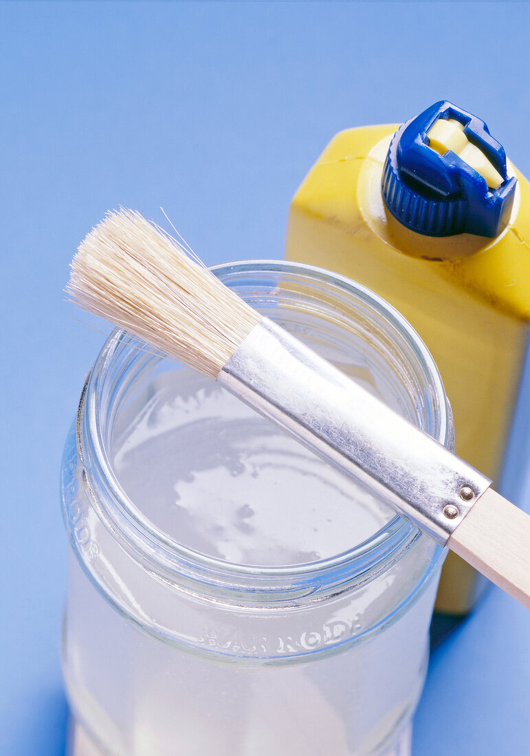 Close-up of paint brush on glass of paste with plastic bottle on side