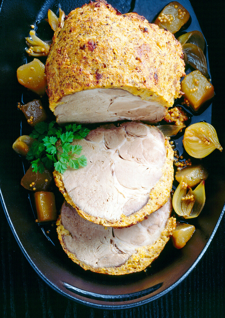 Roast pork with mustard crust and onions in baking dish, overhead view