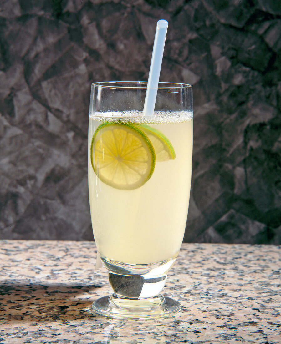 Lemon punch with slice of lime and straw in glass