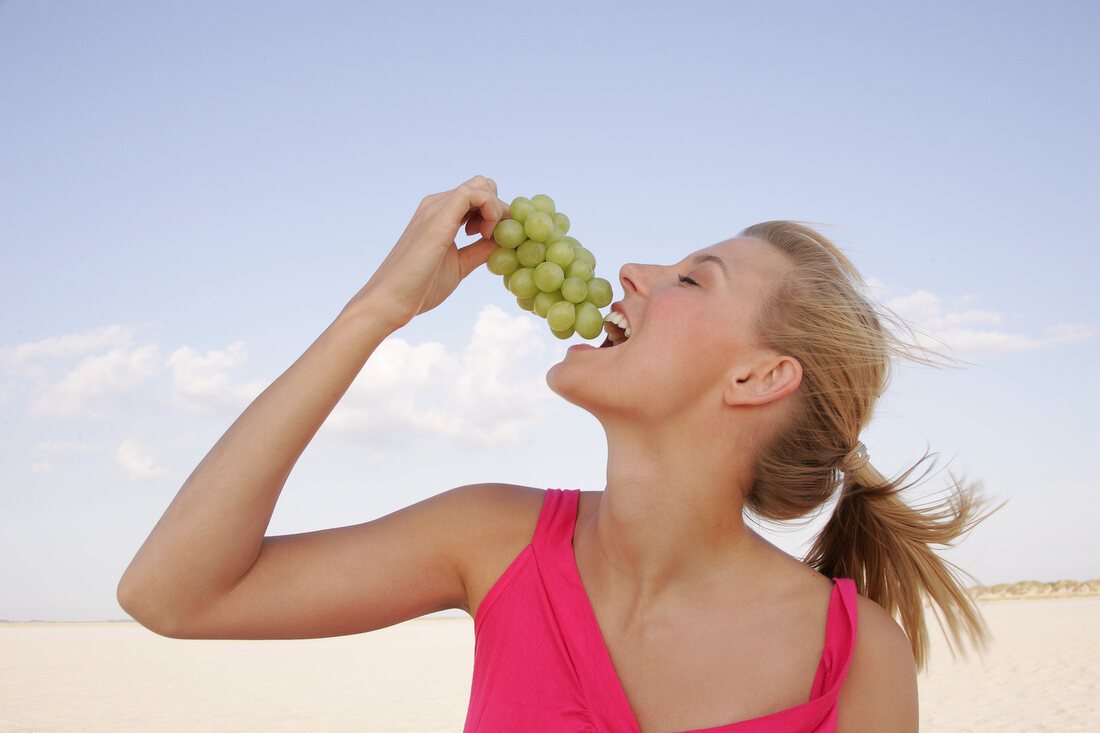 Side view of happy woman holding bunch of grapes near mouth