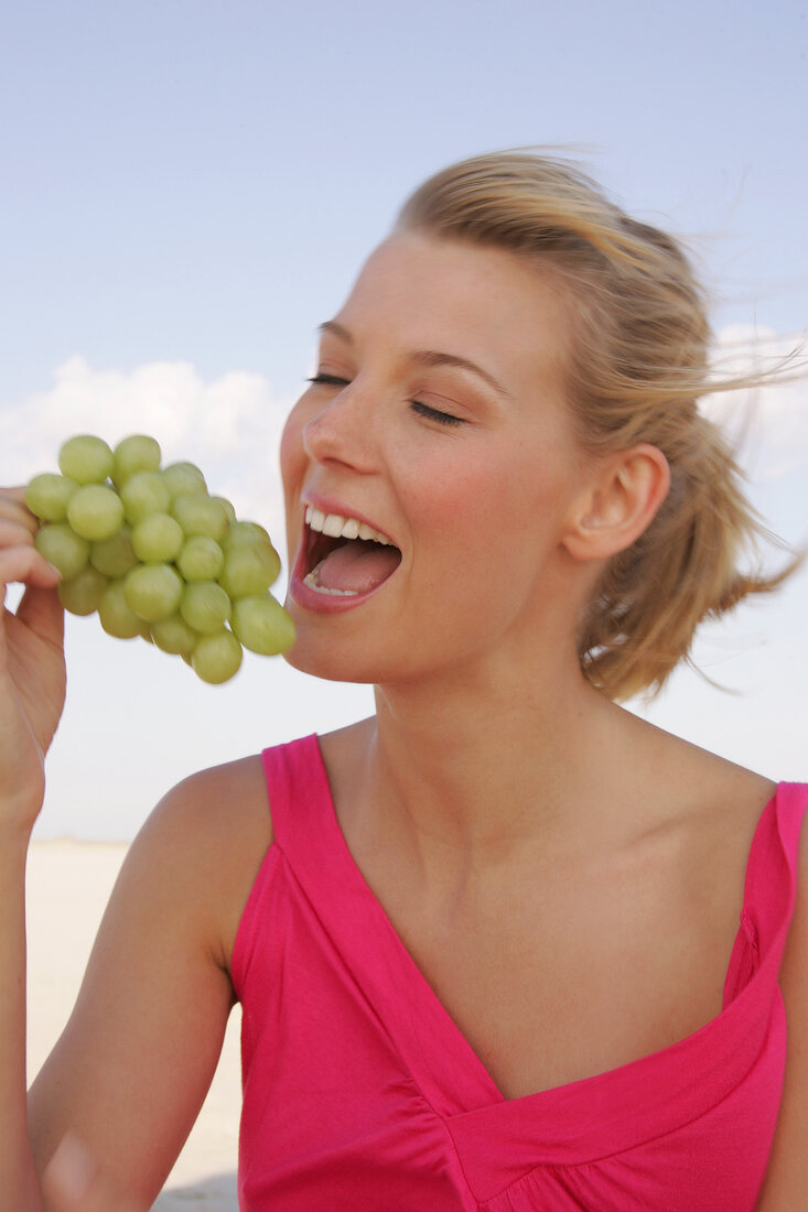 Frau beißt genüsslich in Weintrauben, Profilansicht