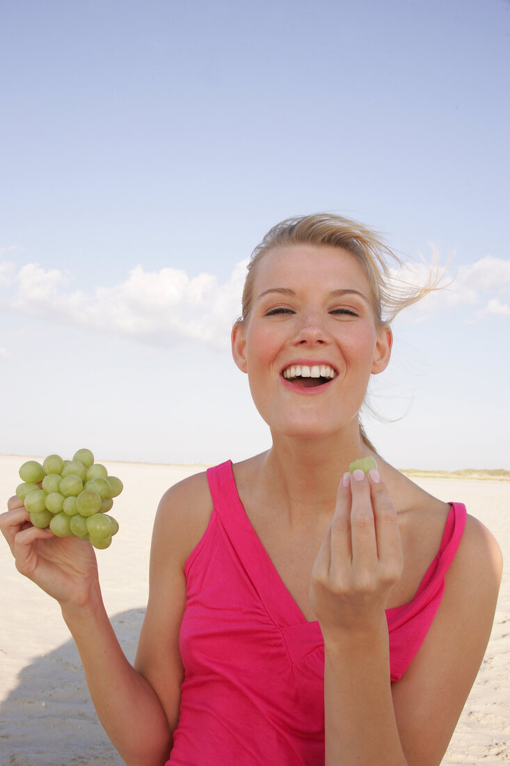 Woman holding a bunch of grapes while eating, smiling