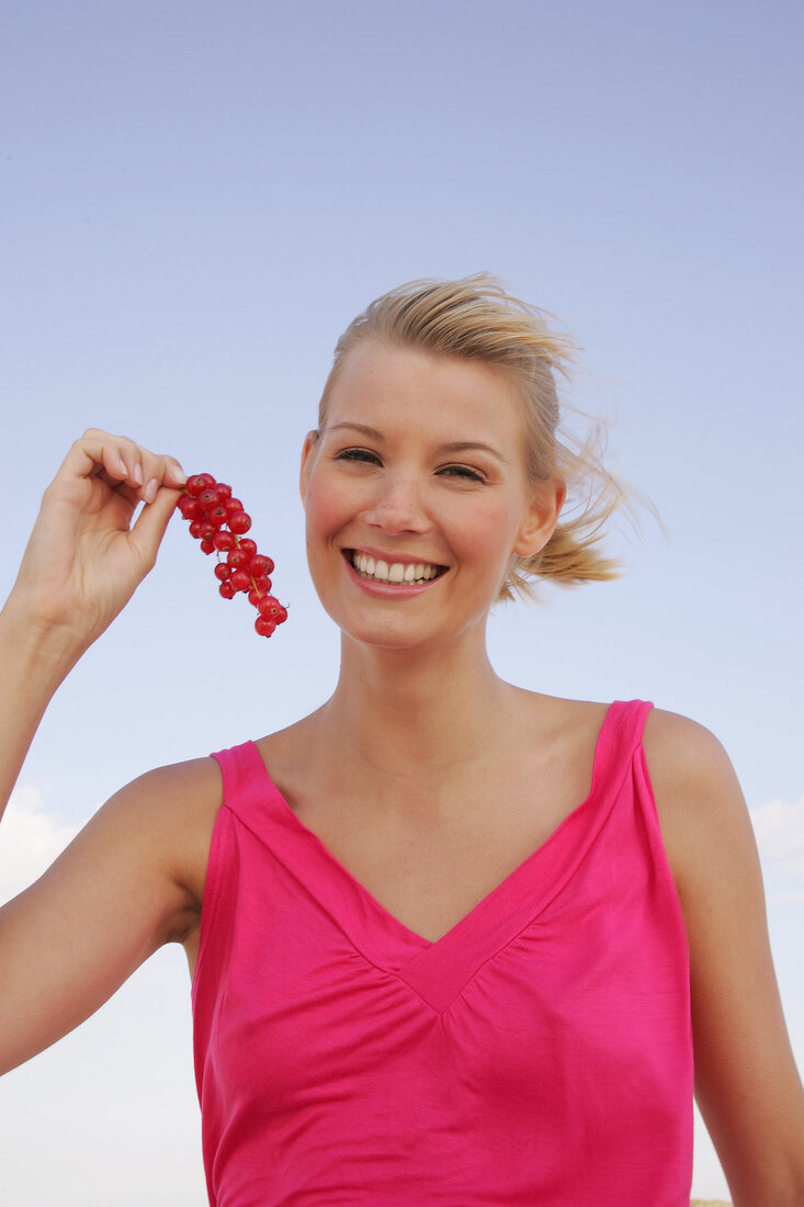 Blonde Frau hat lachend e. Zweig Johannisbeeren in der Hand