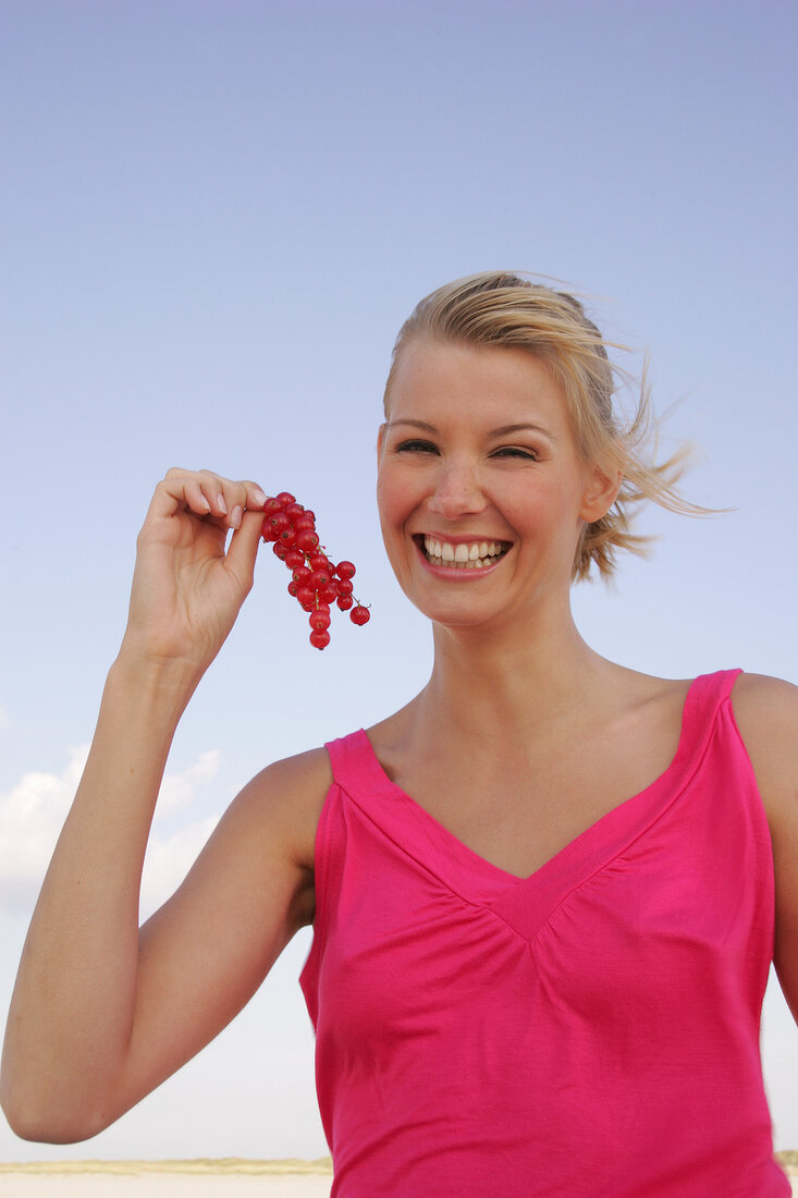 Blonde woman holding a branch of red currants in hand, smiling