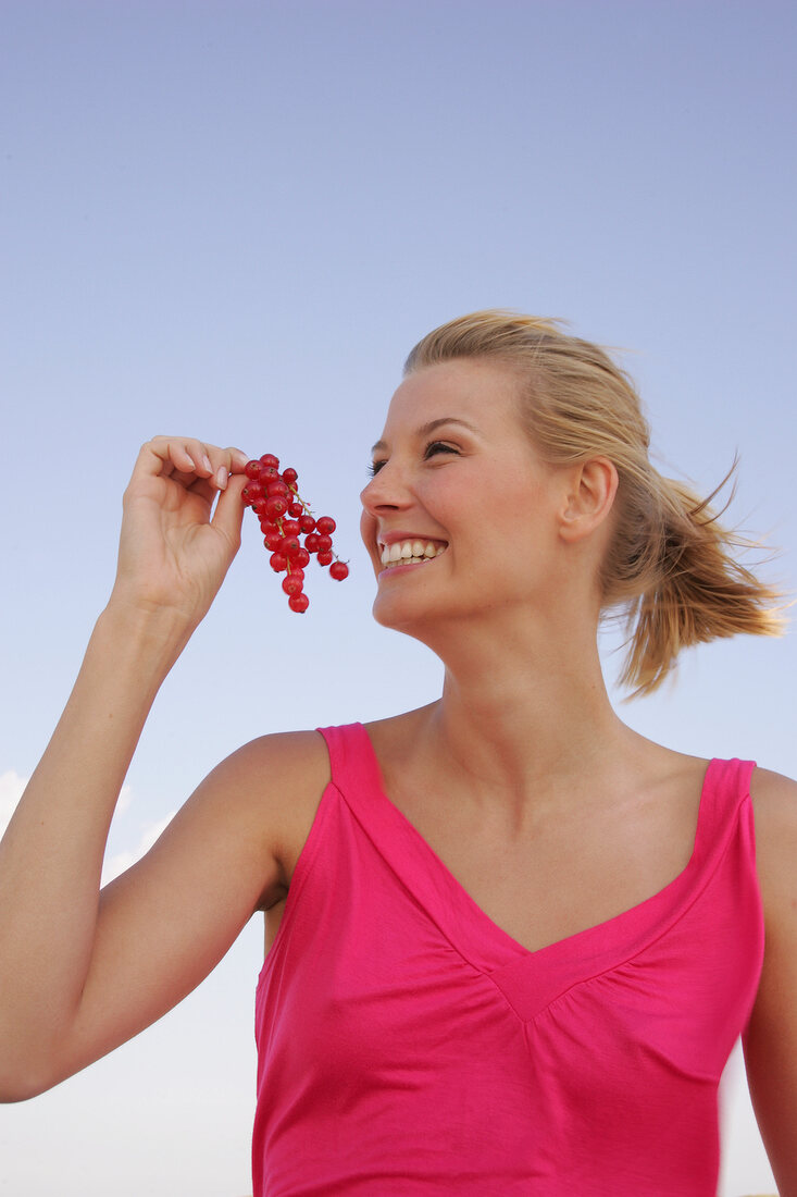 Side view of happy woman holding bunch of red currants