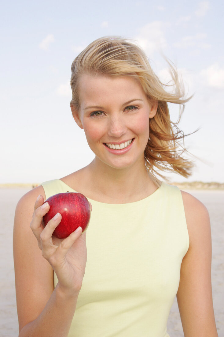 Jennifer Frau am Strand  hält einen Apfel in der Hand, Haare wehen