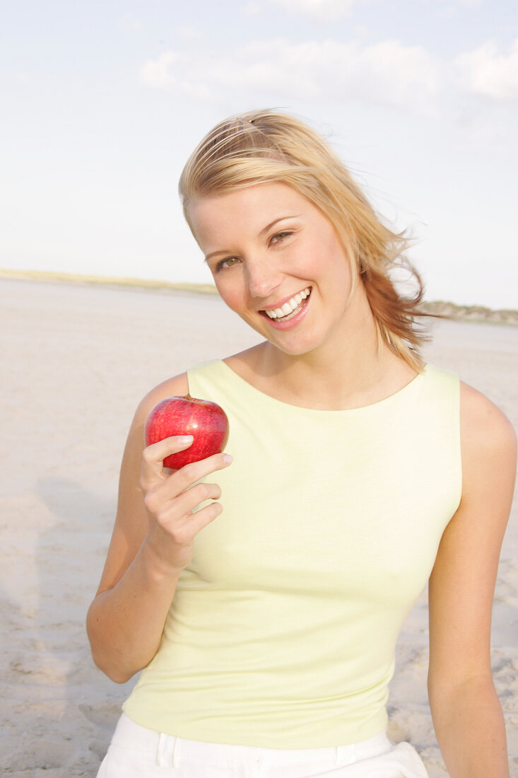 Jennifer Frau am Strand  hält einen Apfel in der Hand, Haare wehen