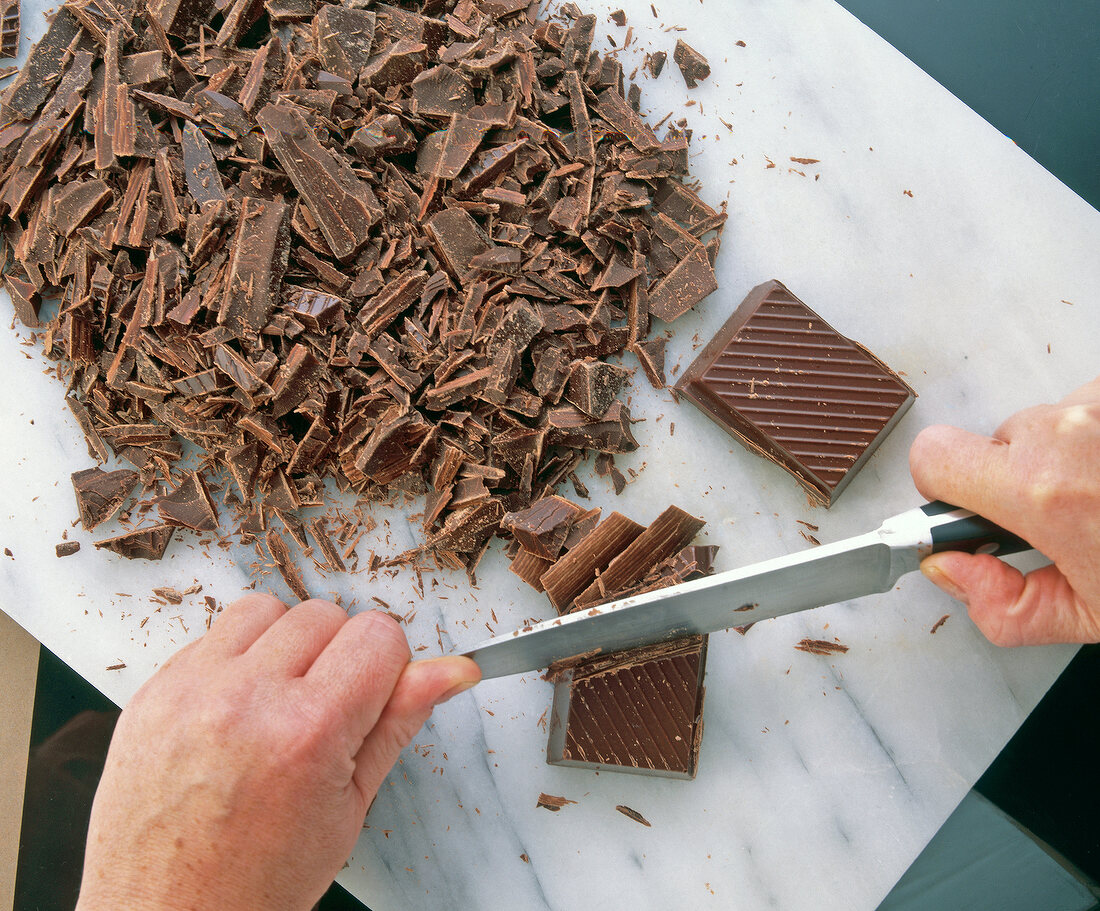 Chopping chocolate with a kitchen knife on cutting board