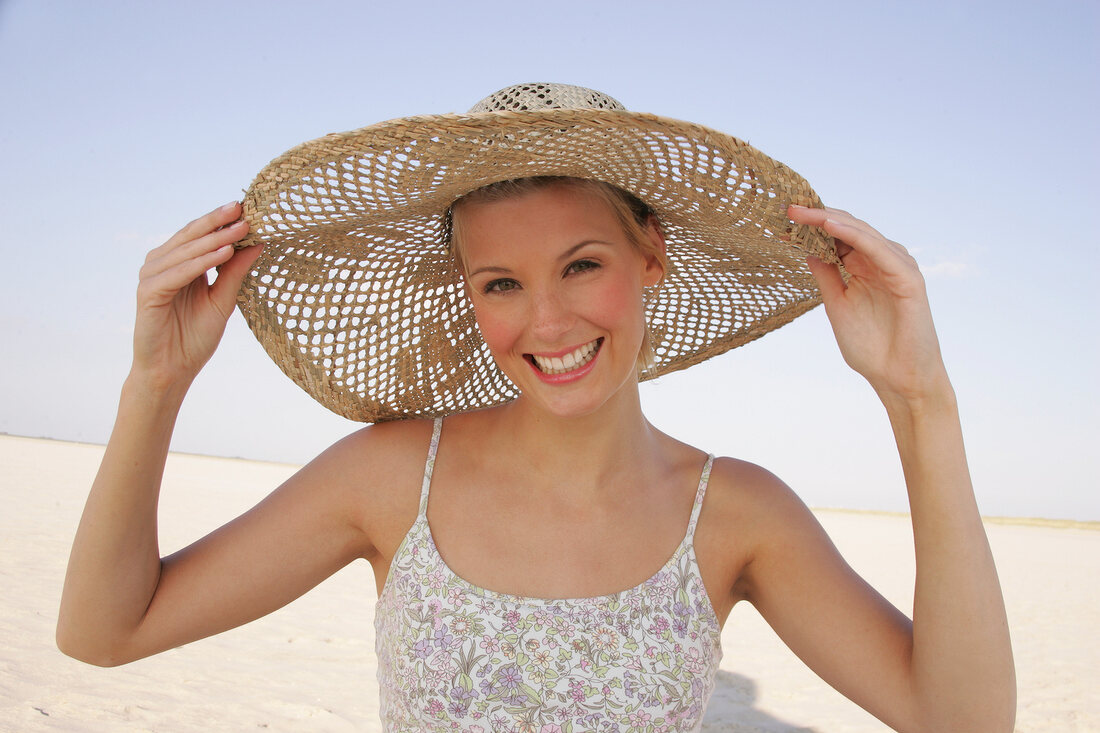 Fröhliche junge Frau am Strand mit einem großen Strohhut
