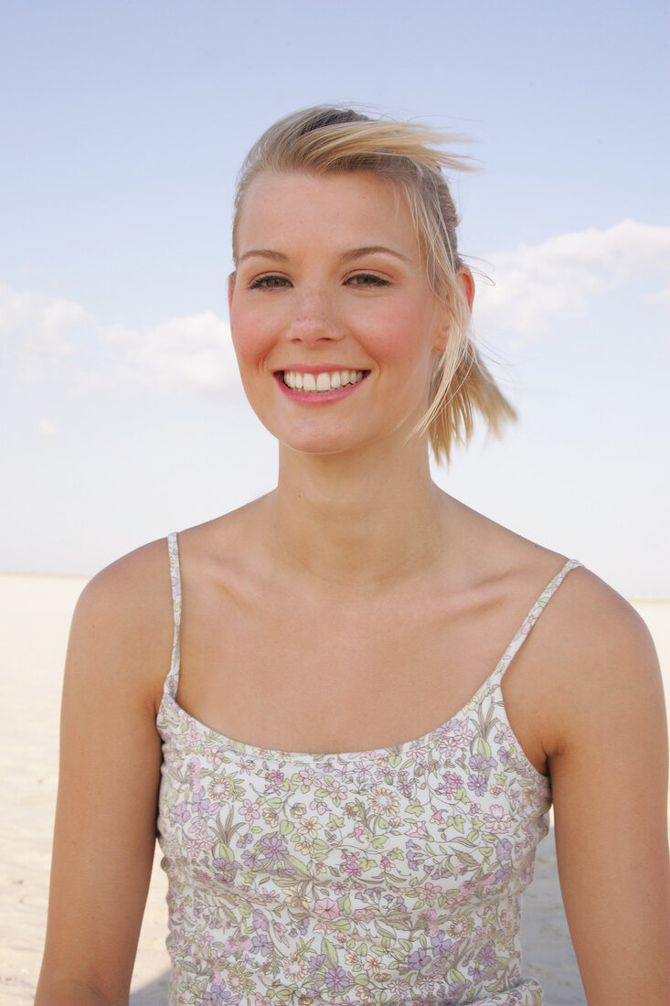 Portrait of beautiful woman in floral pattern dress standing on beach, smiling