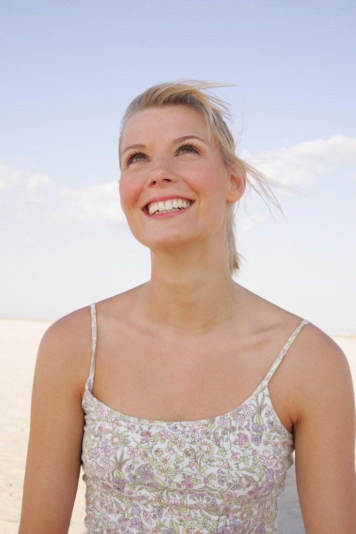 Portrait of beautiful woman in floral pattern dress standing on beach, smiling