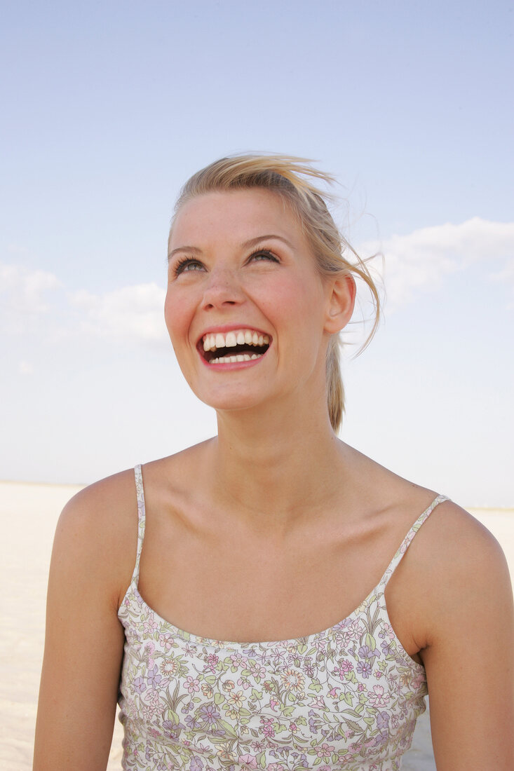 Portrait of beautiful woman in floral pattern dress standing on beach, smiling