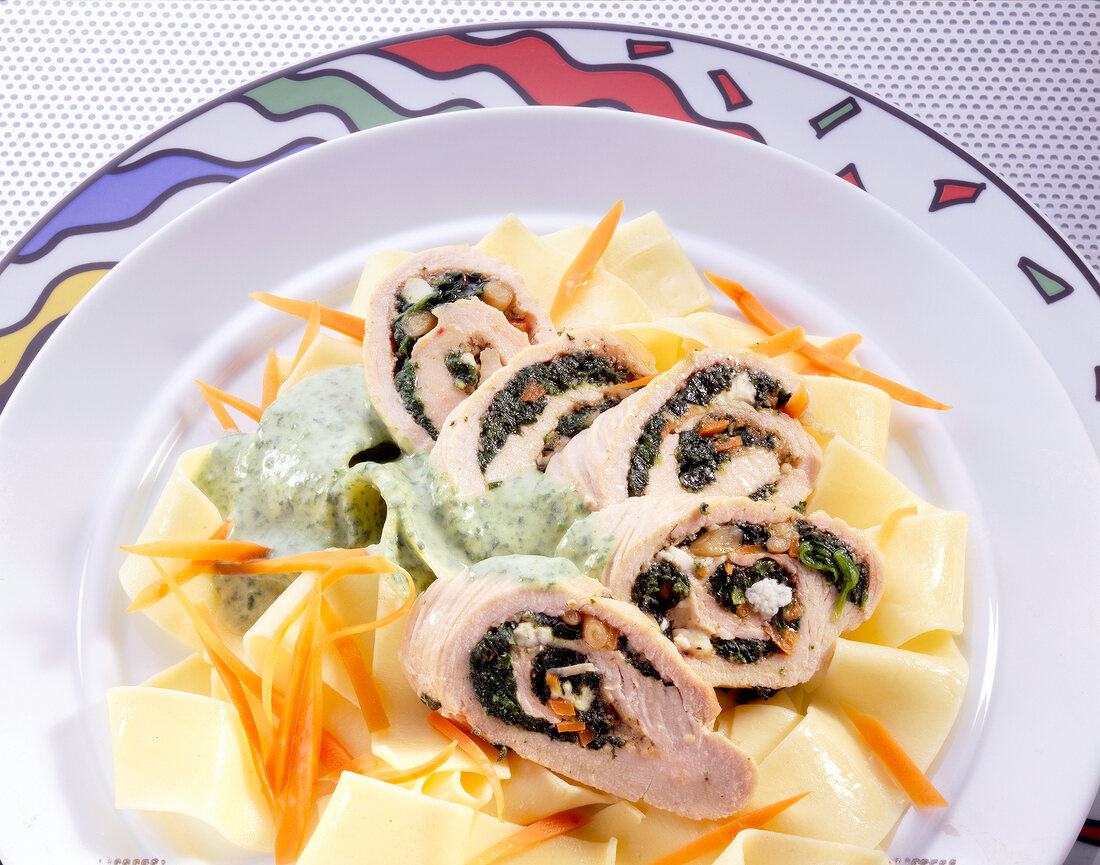 Close-up of turkey rolls with vegetables and pine seeds on ribbon noodles