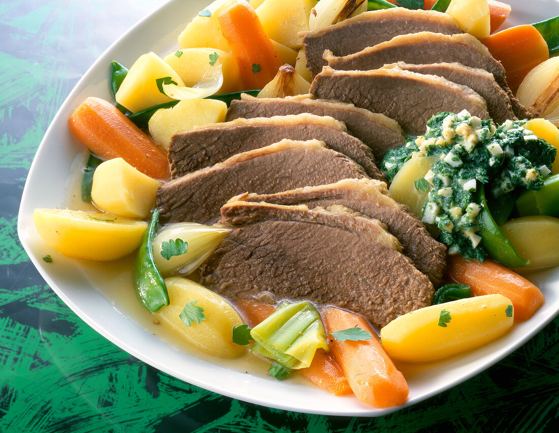 Brisket with carrots, potatoes, sugar peas and herb sauce on plate