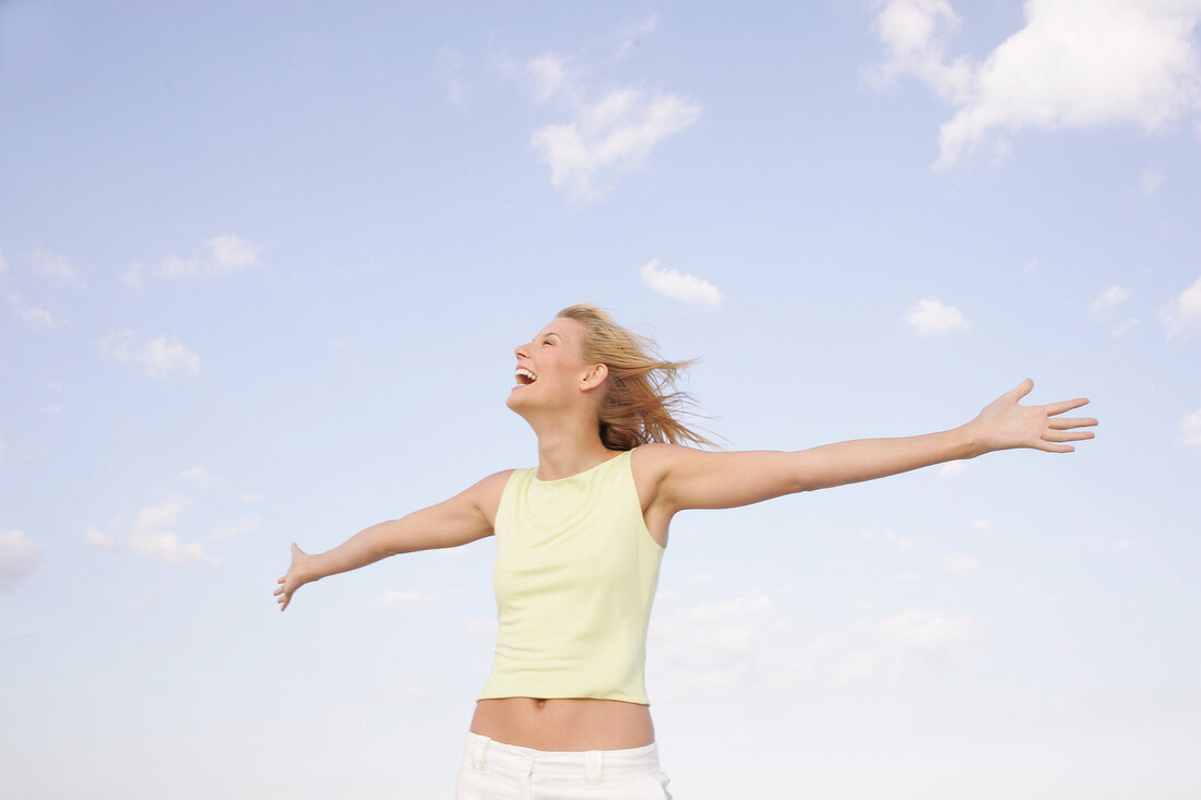 Happy woman with windswept hair with arms outstretched, looking up and laughing