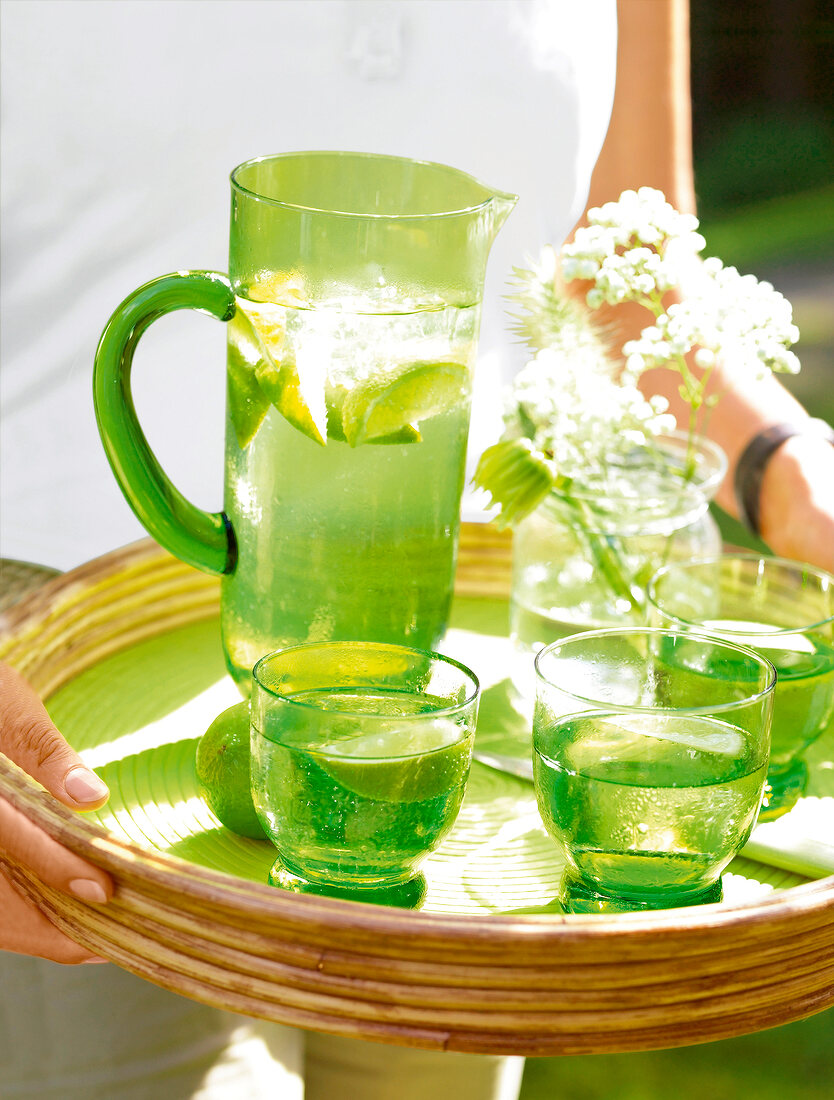 Green jug and glasses with water and lime on wicker tray